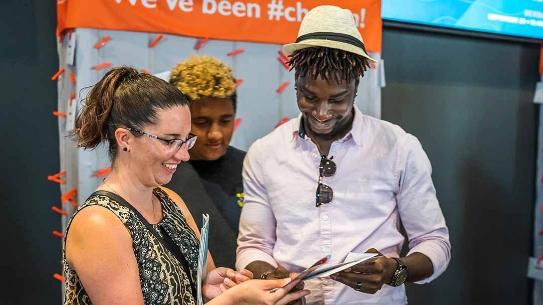 A husband, wife and child look at their paper telling them which child chose them as sponsors and they smile broadly.