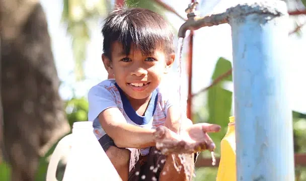 Jory smiles brightly as he washes his hands in with tap water. Siayan, Philippines.