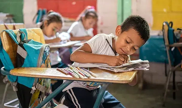 A young boy sitting on his chair drawing on paper.