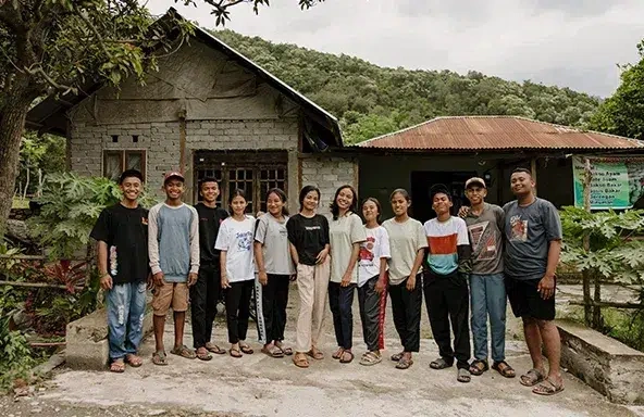 A group of girls and boys stand together in a line outdoors, in front of a building.