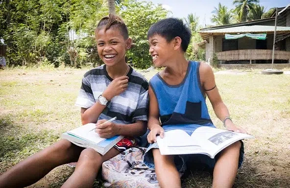 Two boys are sitting on the ground while holding a book.