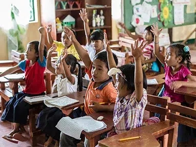 A group of children, raising their hands high, actively participating in a classroom.