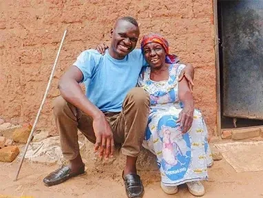 Matieu, a former World Vision sponsored child, sits outside of his childhood home, embracing his grandmother.