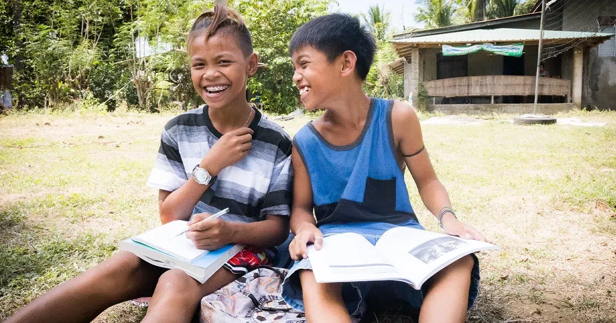 Two boys are sitting on the ground while holding a book.