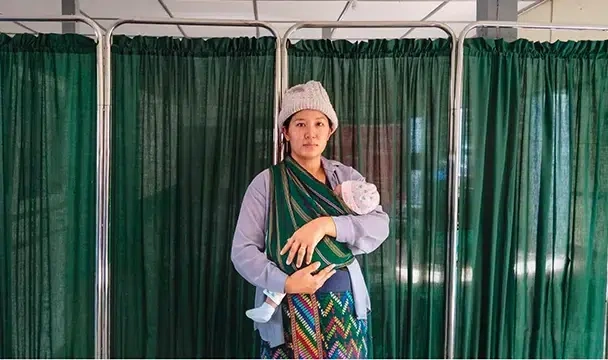 A mother carrying her baby in front of a hospital ward.