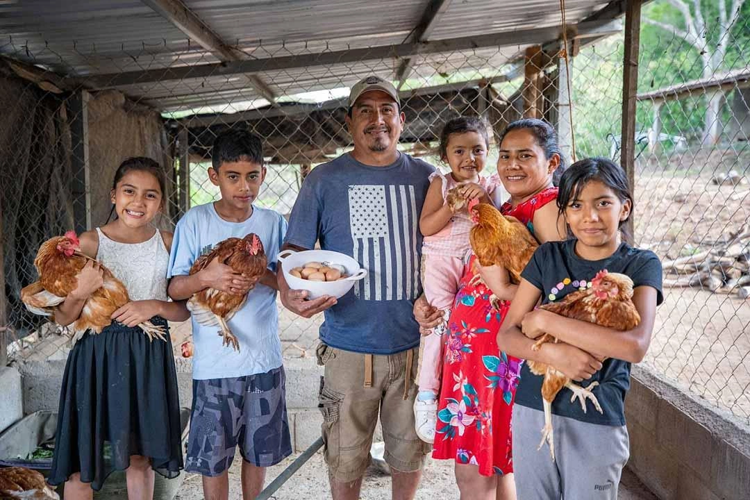 Family proudly stands with chickens that produce eggs for their business that feeds their family.