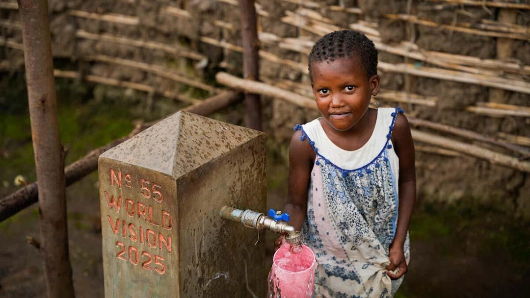 Five year old cautiously smiles while getting water from a public water point.