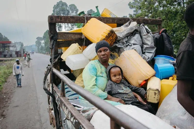 Mother and son travelling in the back of a truck bed with other cargo.