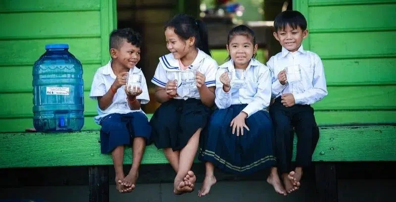 Four tiny children sit nest to a jug of clean water.