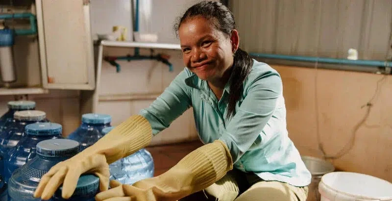 A woman smiles and manages clean water sanitarily with gloves on.