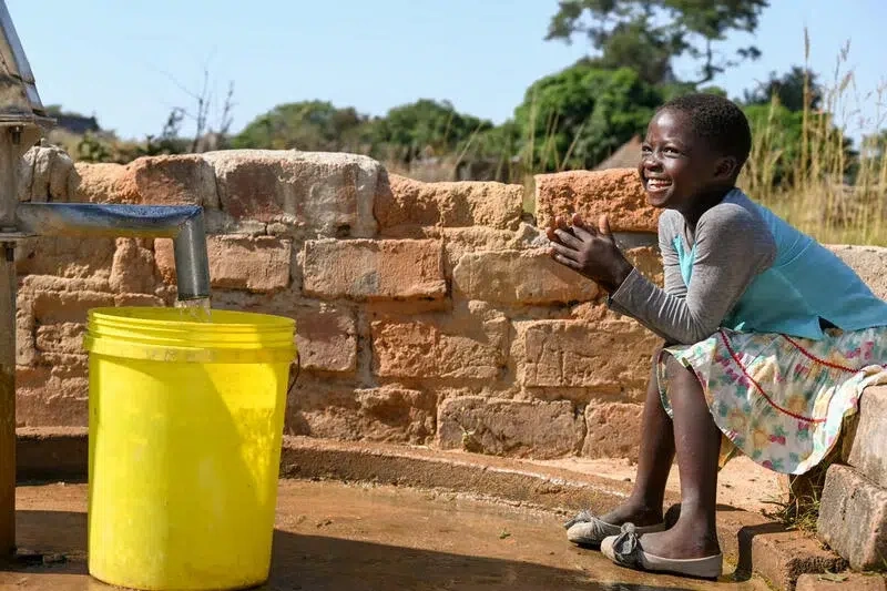 Girls smiles by a clead water bucket and pump.