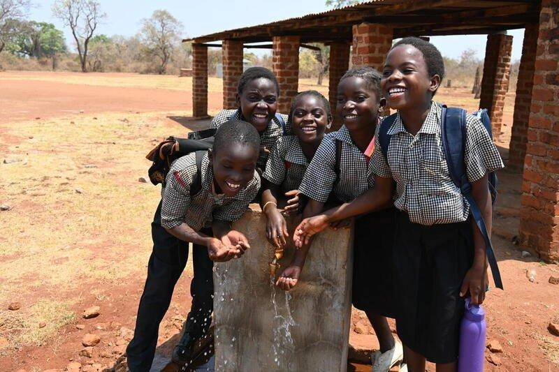 Children stand and smile by a public clean water pump.