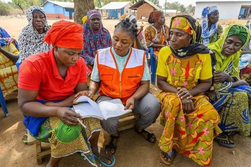 Three women at the front and more at the back learn together with a World Vision Staff.