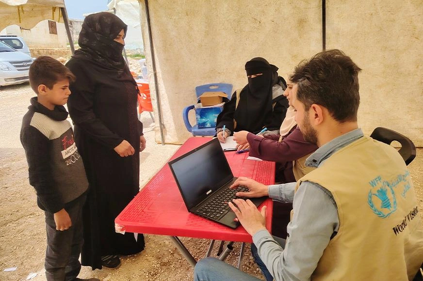 A mother and her son stand at a table to register for assistance in Syria.