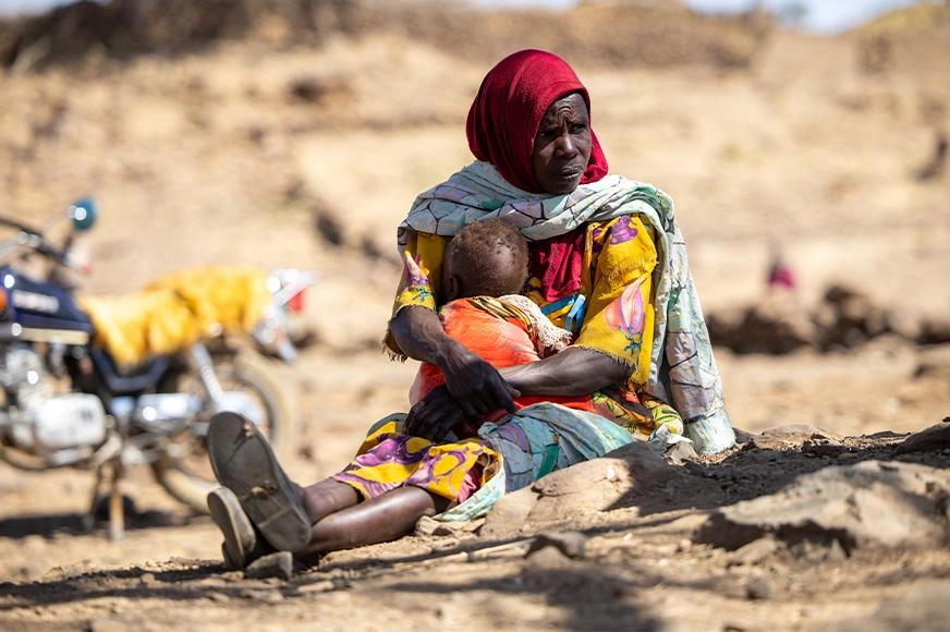 A mother sits on the dusty ground, embracing her malnourished baby.