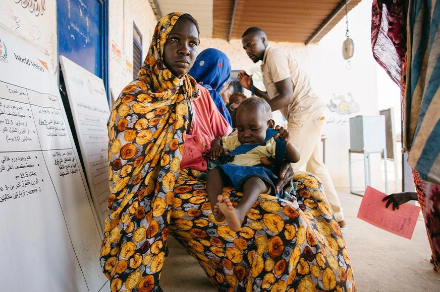 A Sudanese woman holds her baby awaiting medical care at a refugee clinic.