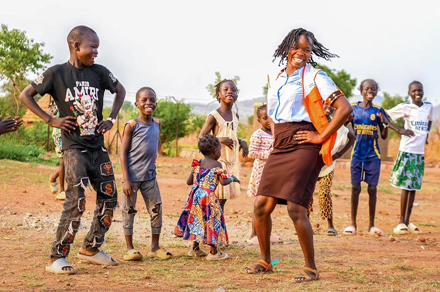 A World Vision worker and several children laugh, smile and dance together in an Ethiopian refugee camp.
