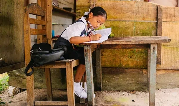 A young girl wearing a school uniform is writing on a notebook.