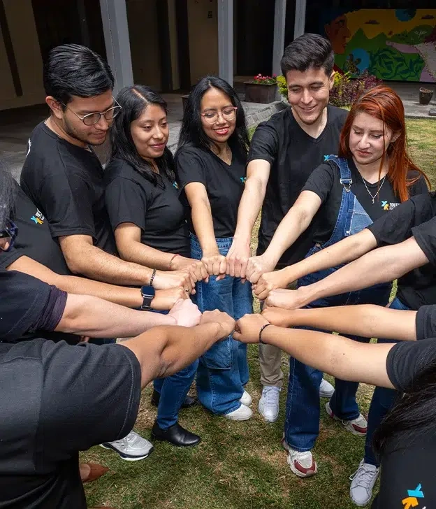 Team members stand in a circle outdoors, joining their fists together during a group activity.