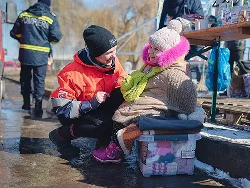 A World Vision staff is talking to a little girl sitting on a box of clothes at the Siret border in Romania.