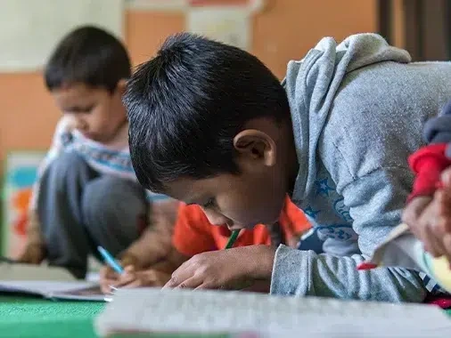 Child writing on desk at school.