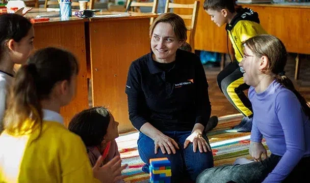 A World Vision staff sits on the floor surrounded by children.