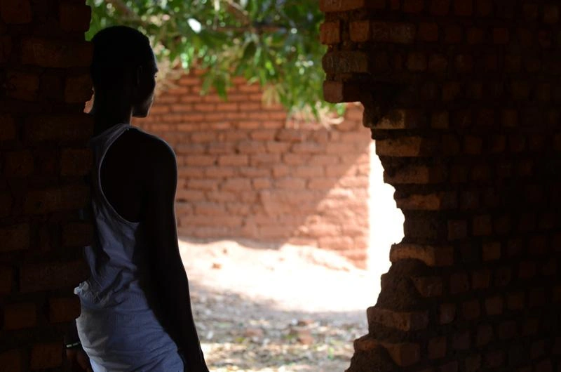 Un jeune homme, ancien enfant-soldat au Soudan du Sud, est adossé à un mur de briques en ruine.