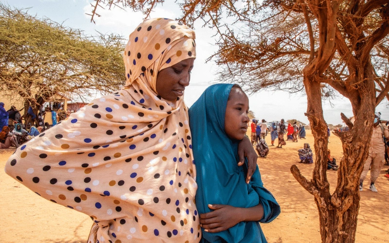 Une femme et une fillette se tiennent côte à côte à l’extérieur, dans un camp accueillant des personnes déplacées en Somalie en raison de menaces telles que les changements climatiques.
