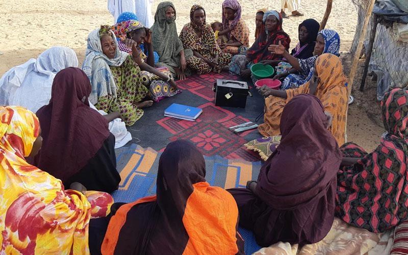 Un groupe de femmes appartenant à un groupe d'épargne est assis en cercle autour d'un coffret de sécurité.