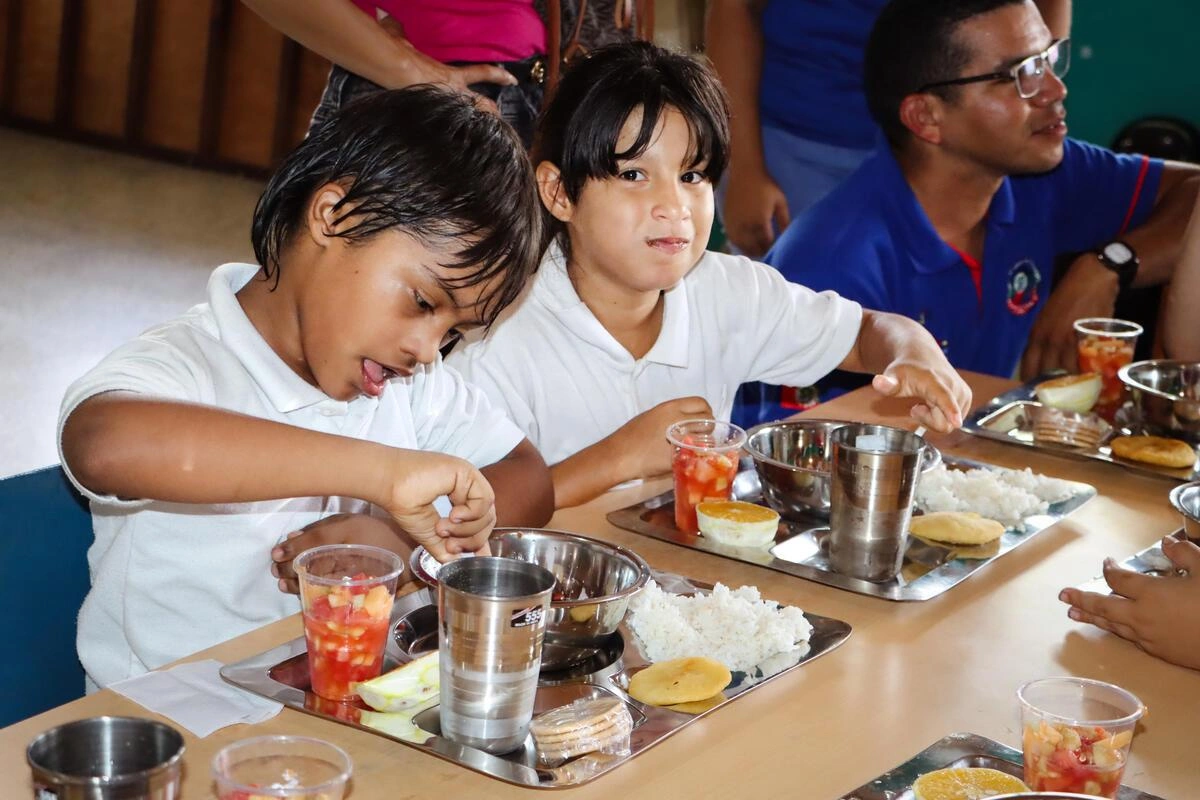 Des enfants vêtus de chemises blanches d'uniforme se régalent de leur dîner d'école (Venezuela, 2025)