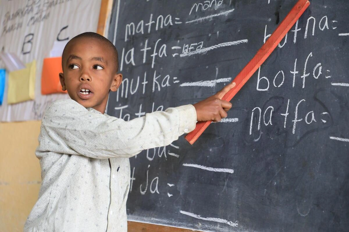 Un jeune enfant tenant un bâton pour pointer devant un tableau noir (Éthiopie, 2025)