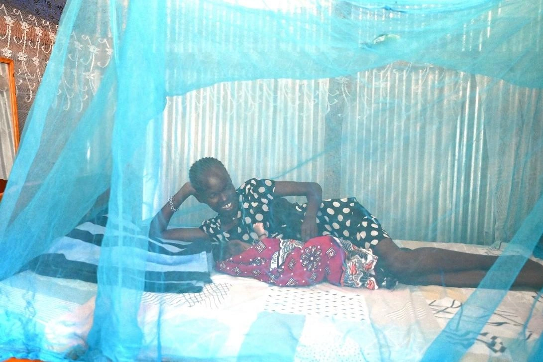 Dans le comté de Turkana, au Kenya, une nouvelle maman allaite son bébé en position couchée sur le côté, sous une moustiquaire bleue.