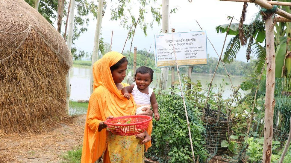 À Islampur, au Bangladesh, une femme tient un bébé sur sa hanche tout en ramassant les produits de son potager.