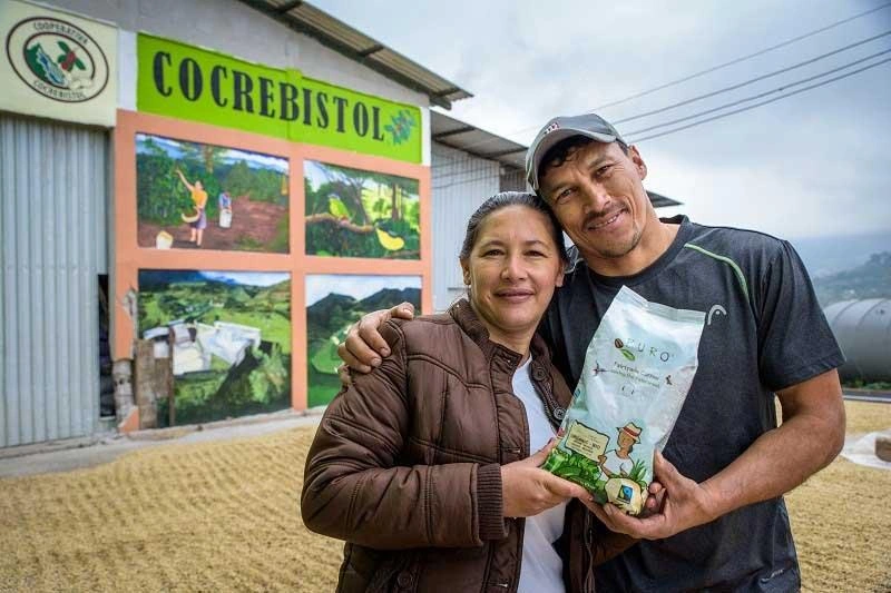 Au Honduras, un homme et une femme tiennent fièrement un sac de grains de café. Ils se tiennent devant leur commerce.
