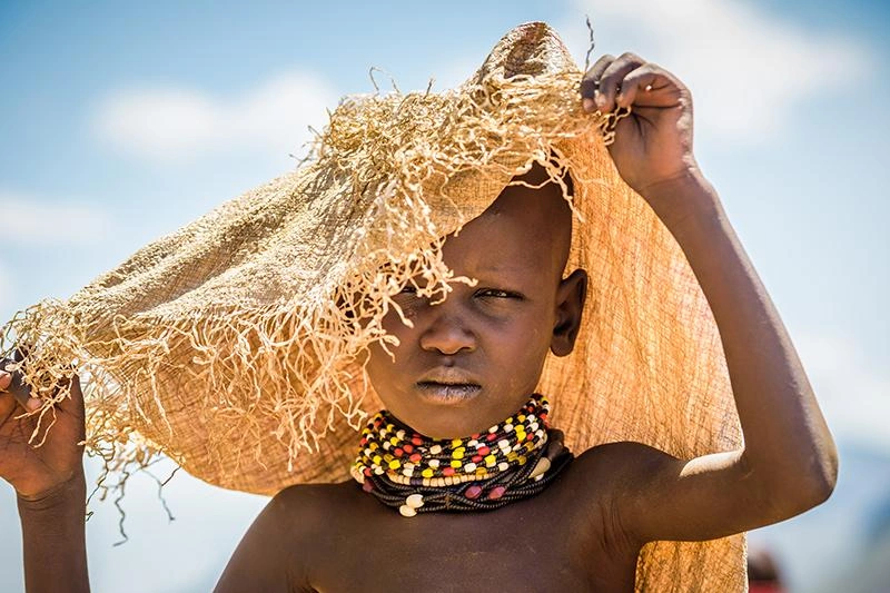 Une jeune fille se protège du soleil à l'aide d'un sac qui servait à transporter la nourriture reçue lors d'une distribution.