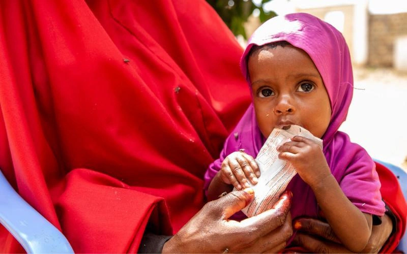 À Baidoa, en Somalie, une toute jeune fillette est tenue dans les bras d’une femme tandis qu’on lui donne à manger pour lutter contre la malnutrition grave.