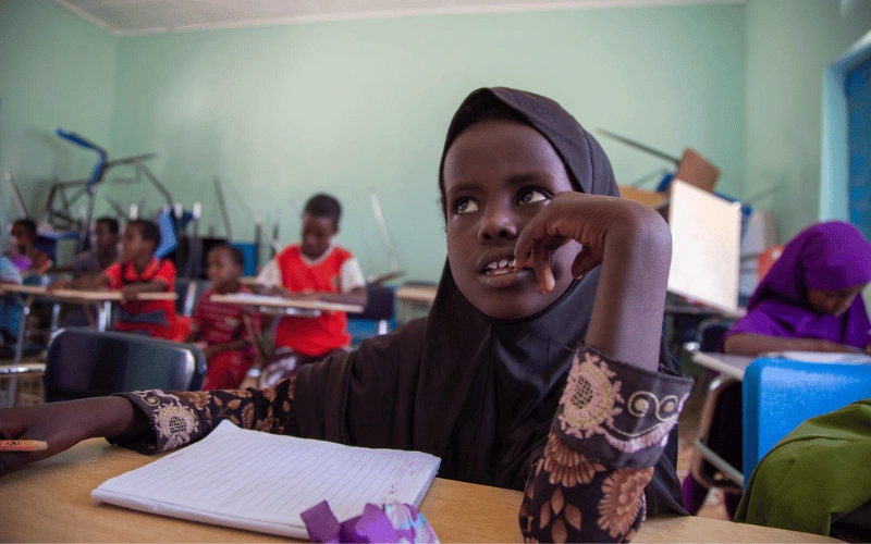 Une jeune Somalienne portant un hijab, assise à son pupitre dans sa salle de classe, avec un crayon et un cahier.