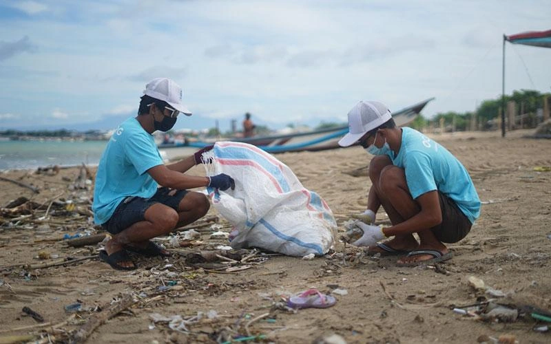 Deux hommes de l'organisme « The Ocean Clean-up Group », à Bali, en Indonésie, s'accroupissent pour ramasser des déchets sur la plage.