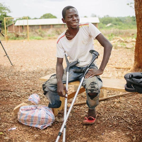 Un homme centrafricain, qui n'a qu'une jambe, est assis sur un banc, ses béquilles à la main.