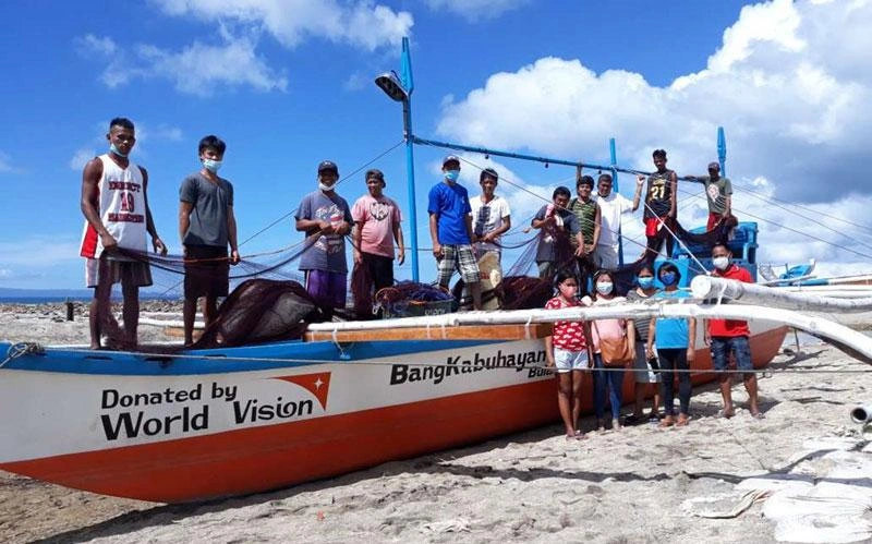 Un groupe d'adultes et d'enfants se tient sur un bateau de pêche et à proximité de celui-ci, sur une plage aux Philippines.