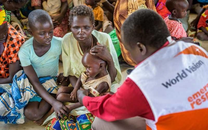 Un travailleur humanitaire portant un gilet d’intervention d’urgence de World Vision prend les mesures du bras d’un jeune enfant afin de détecter un éventuel cas de malnutrition.