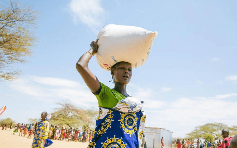 Une femme marche en portant un sac de céréales sur la tête.