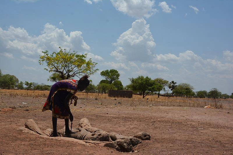 Une jeune femme de dix-neuf ans se penche pour puiser de l'eau dans un fossé au milieu d'un paysage aride.