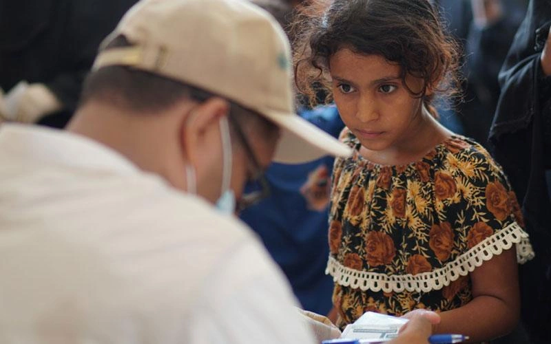 Au Yémen, une adolescente montre un document à un travailleur humanitaire qui porte un masque.