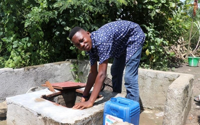 À Tejan, en Sierra Leone, un homme est penché au-dessus d’un puits d’eau douce, un seau à ses côtés.
