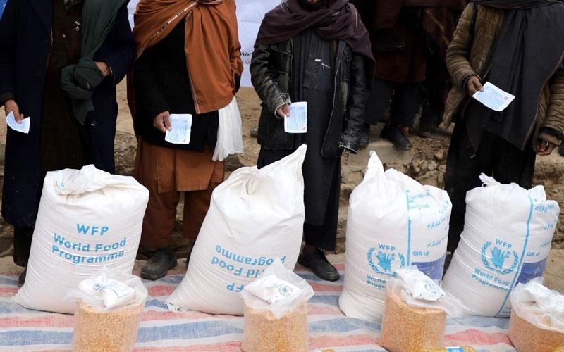 Photo recadrée montrant une file d’hommes debout qui font la queue pour recevoir leurs rations alimentaires.