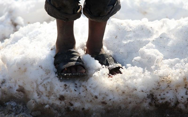 Gros plan sur les pieds d’un enfant debout dans la neige, ne portant rien d’autre que des sandales.