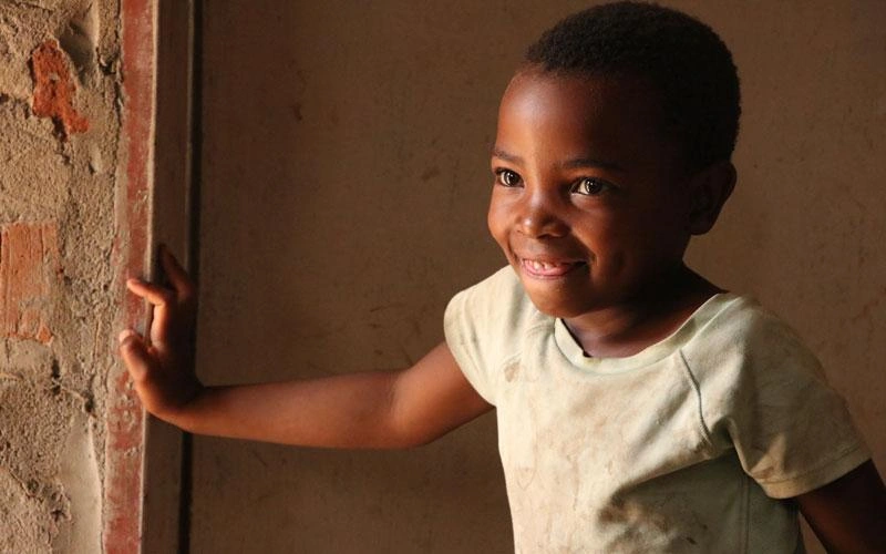 Une jeune Zambienne sourit sur le seuil d'une porte.