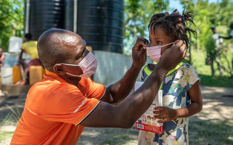 Un Haïtien aide un jeune enfant à mettre son masque.