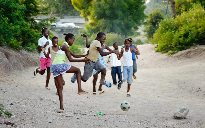 Un groupe d'enfants haïtiens joue au soccer à l'extérieur.
